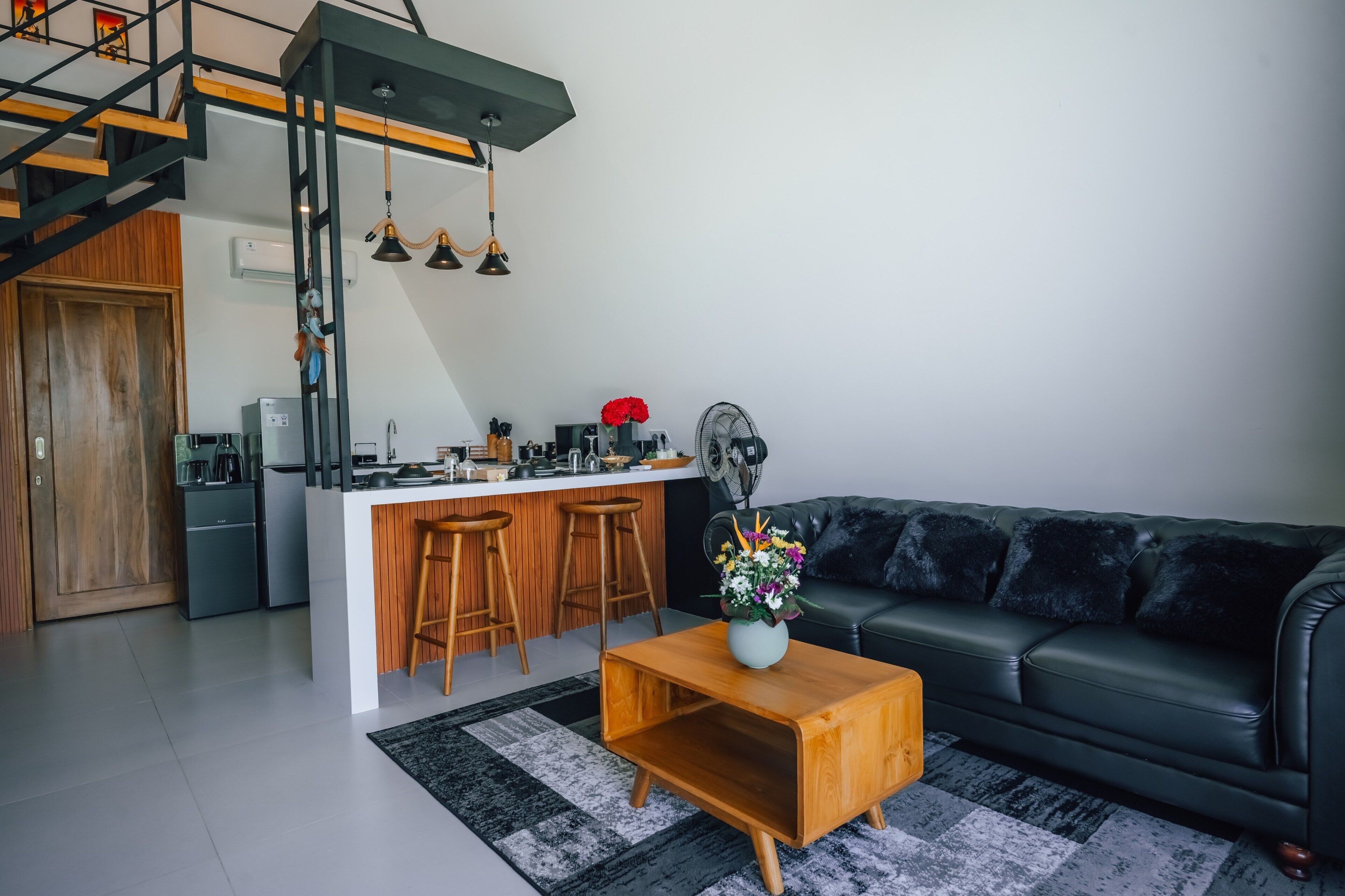 Eine moderne Küche mit einer zentralen Kochinsel, einem Essbereich mit Hockern, einem schwarzen Ledersofa und einem Holztisch.