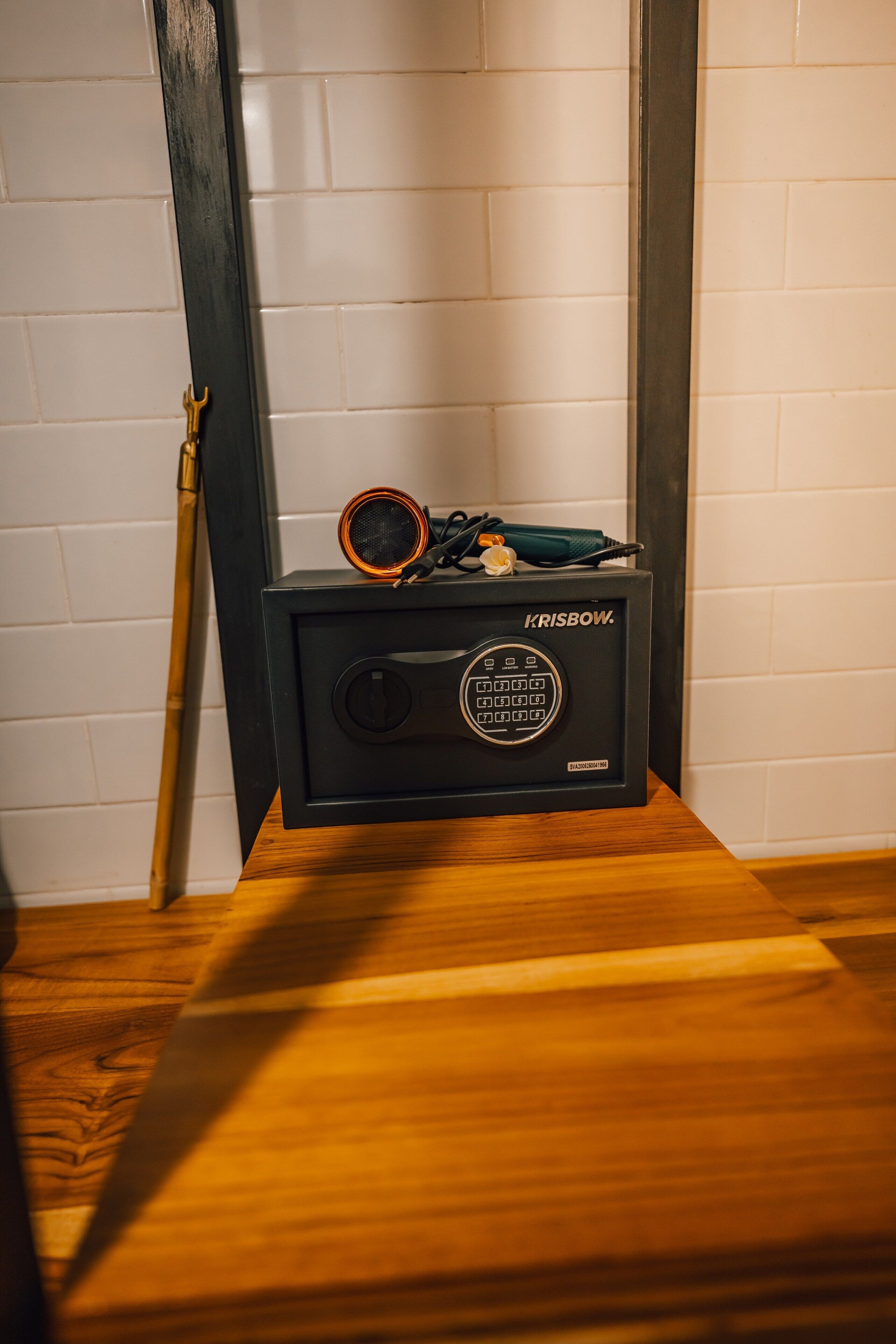 A black speaker with a circular grill and a control panel on a wooden surface against a white tiled wall.