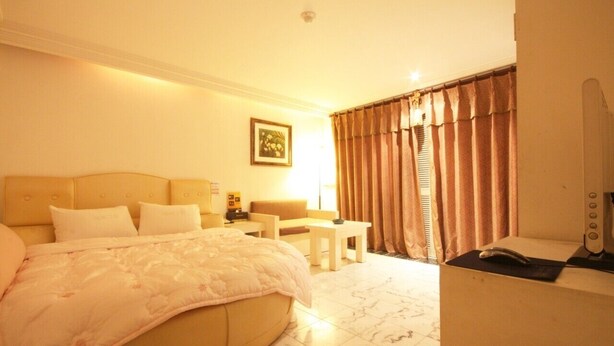 Habitación de hotel con cama, escritorio, silla, lámpara y ventana con cortinas.