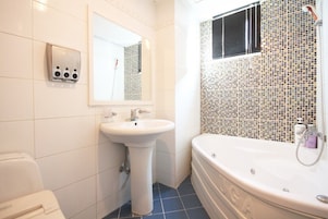 Un baño con lavamanos blanco, espejo, inodoro y bañera con mosaicos.