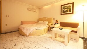 Una habitación de hotel con una cama redonda, un sofá, una mesita y una mesita de noche.