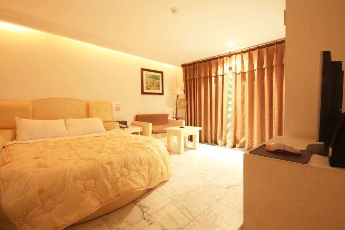 A hotel room with a bed, a desk, a chair, a small table, and a window with curtains.