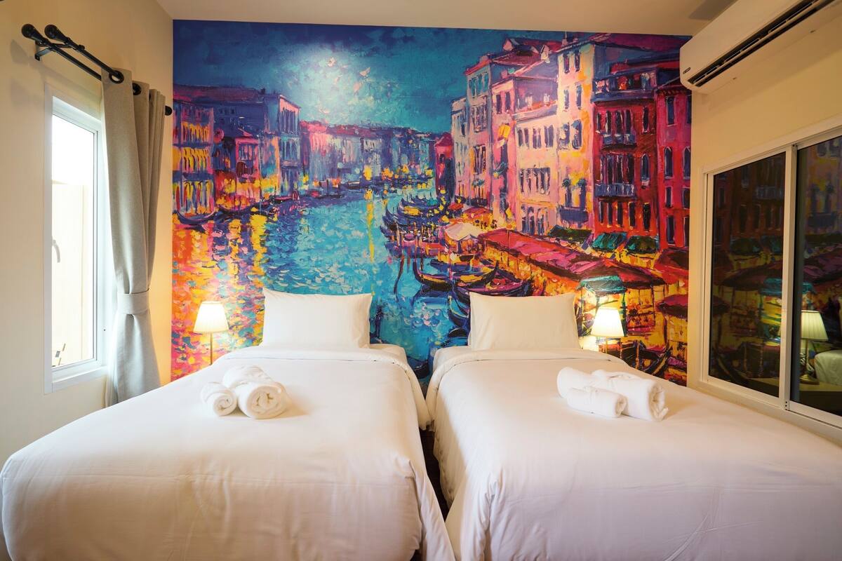 Habitación de hotel con dos camas, un ventanal grande y un cuadro con una vista vibrante de la ciudad.