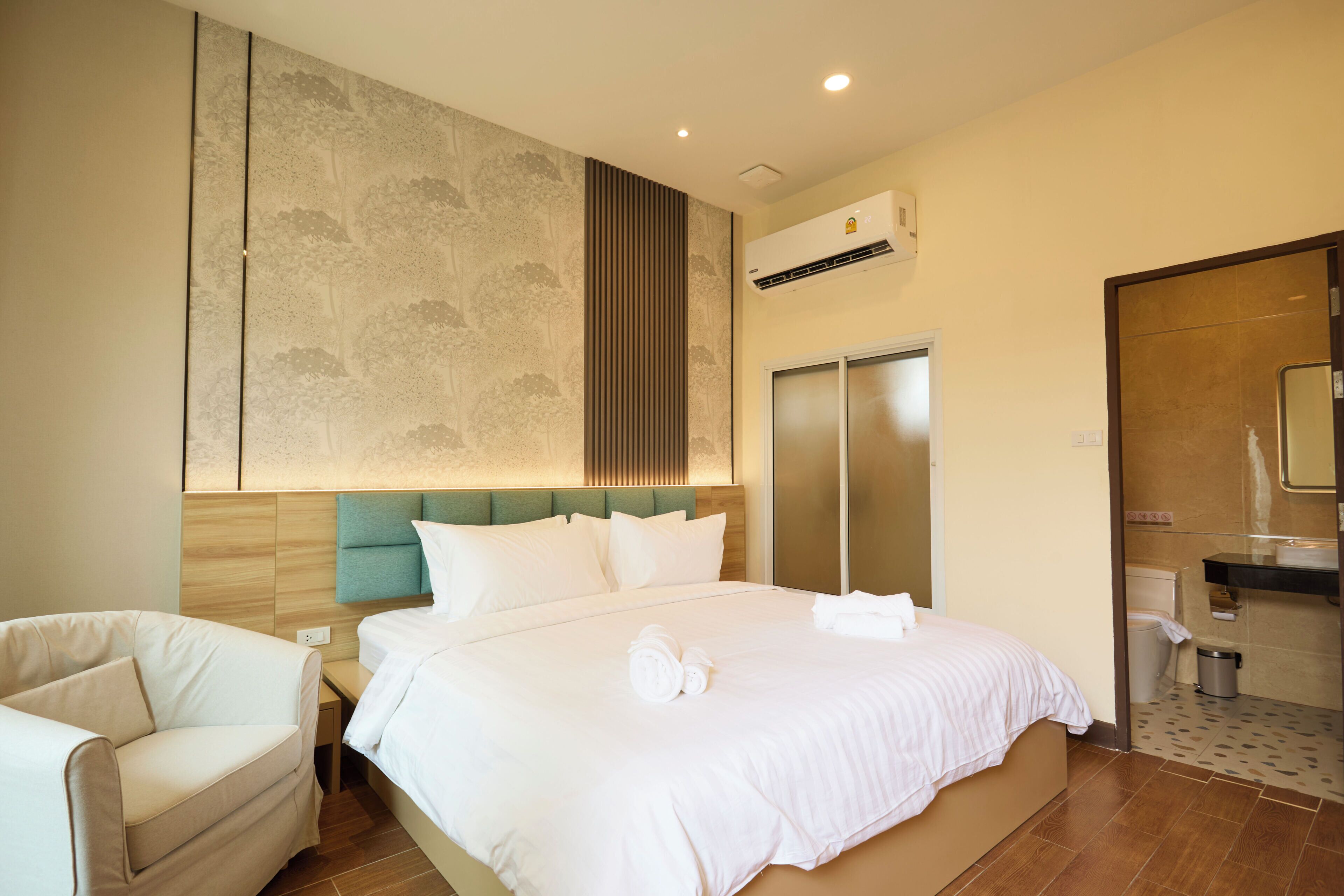 A hotel room with a large bed, a chair, a wardrobe, and a bathroom.