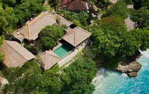 Luftaufnahme eines Küsteneigentums mit mehreren Gebäuden, einem Swimmingpool und üppiger Vegetation.