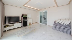 Una sala de estar moderna con un televisor de pantalla plana, una cafetera, un sofá con almohadones y una puerta de vidrio que da a un baño.