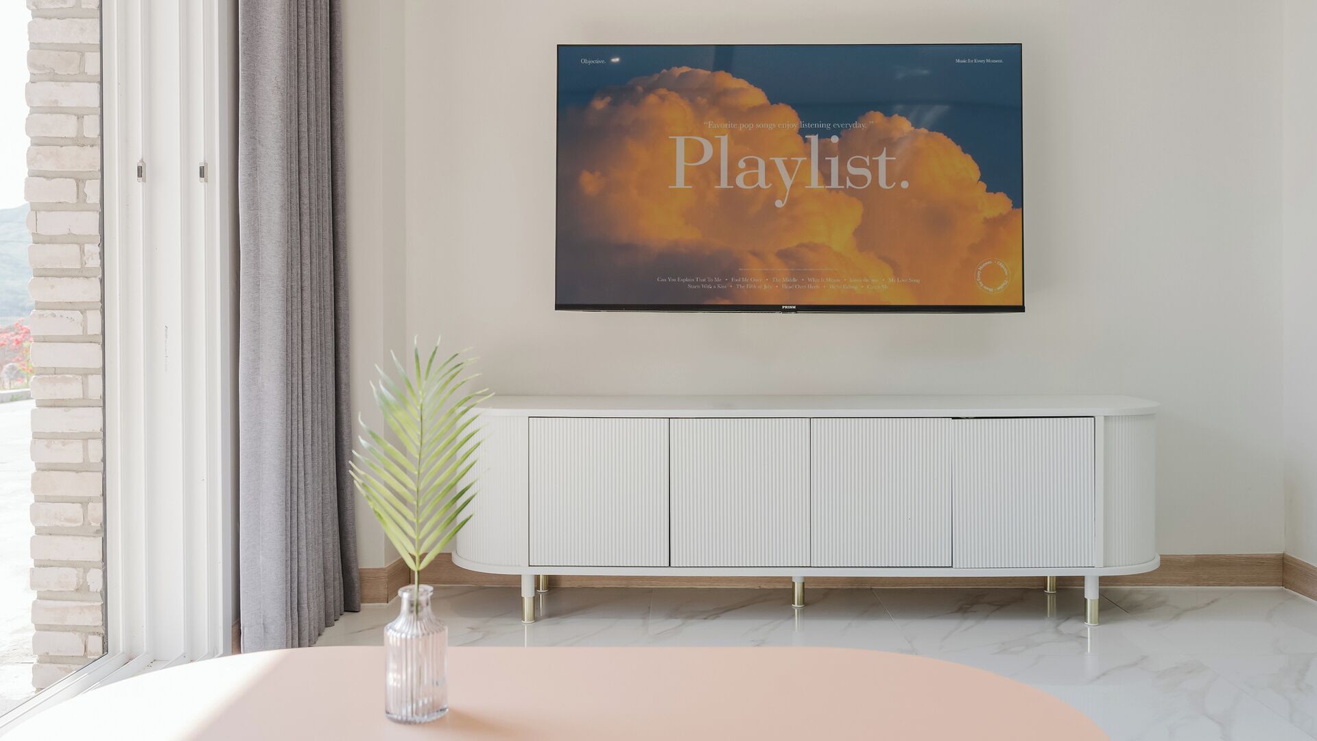 A modern living room with a large flat-screen TV mounted on the wall displaying a playlist.