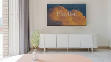 A modern living room with a large flat-screen TV mounted on the wall displaying a playlist.