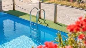 Una piscina con escaleras de metal, rodeada de una zona pavimentada y césped.