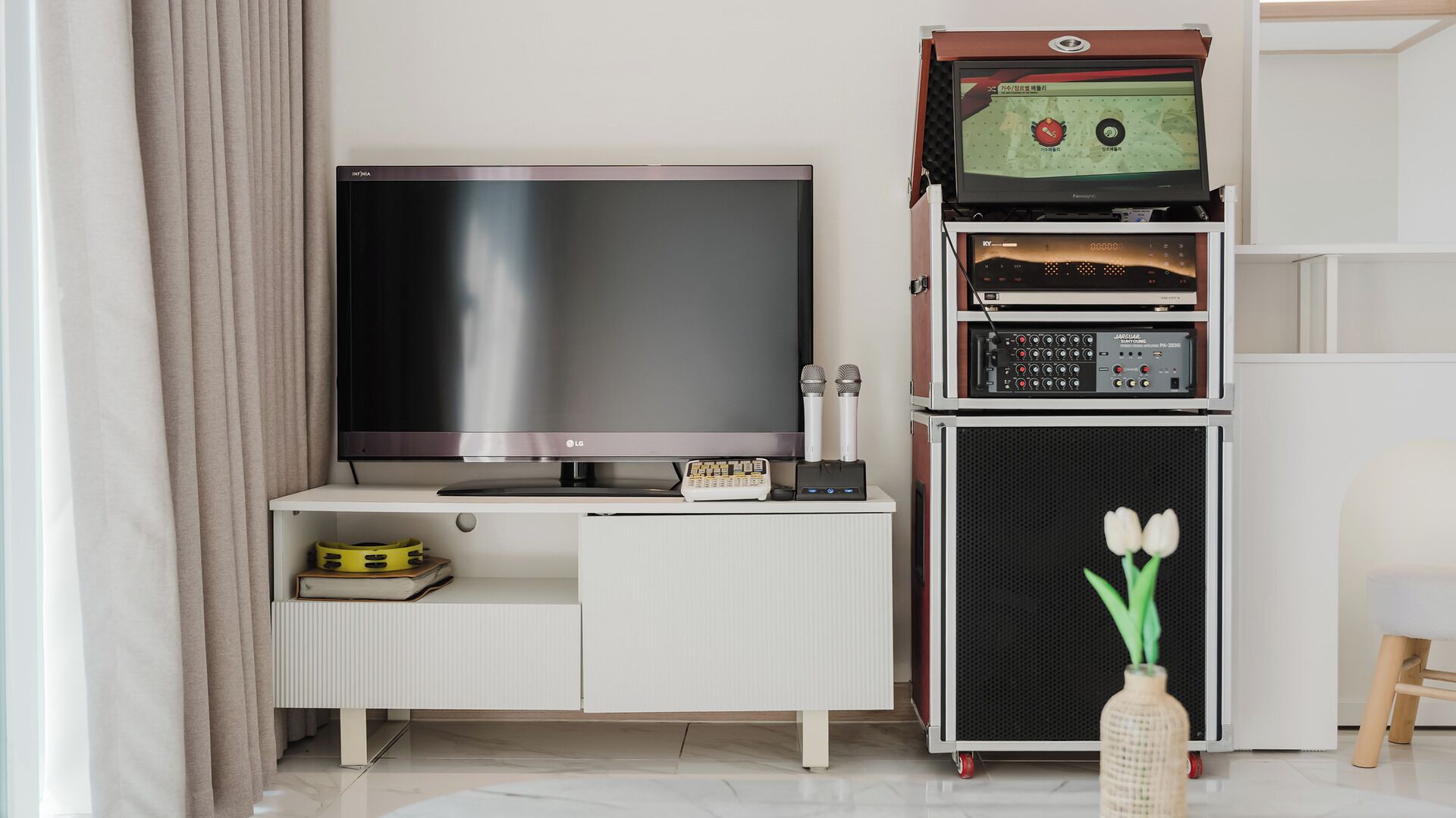 Una sala de estar moderna con una televisión de pantalla plana, un sistema de sonido y una mesita con un libro y un objeto amarillo.