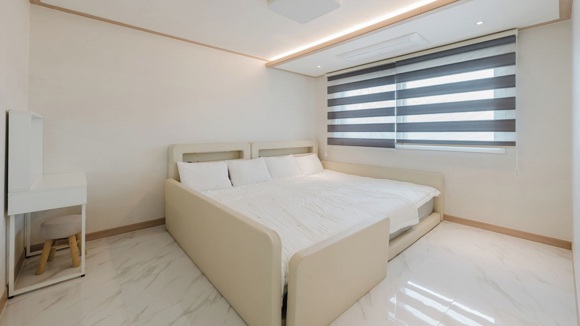 A modern bedroom with a large bed, a bedside table, and a window with blinds.