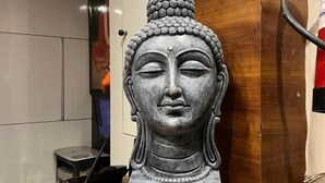 Una estatua sobre un pedestal de madera en una habitación con un cartel que indica la hora de registro y un cargo adicional por GST.