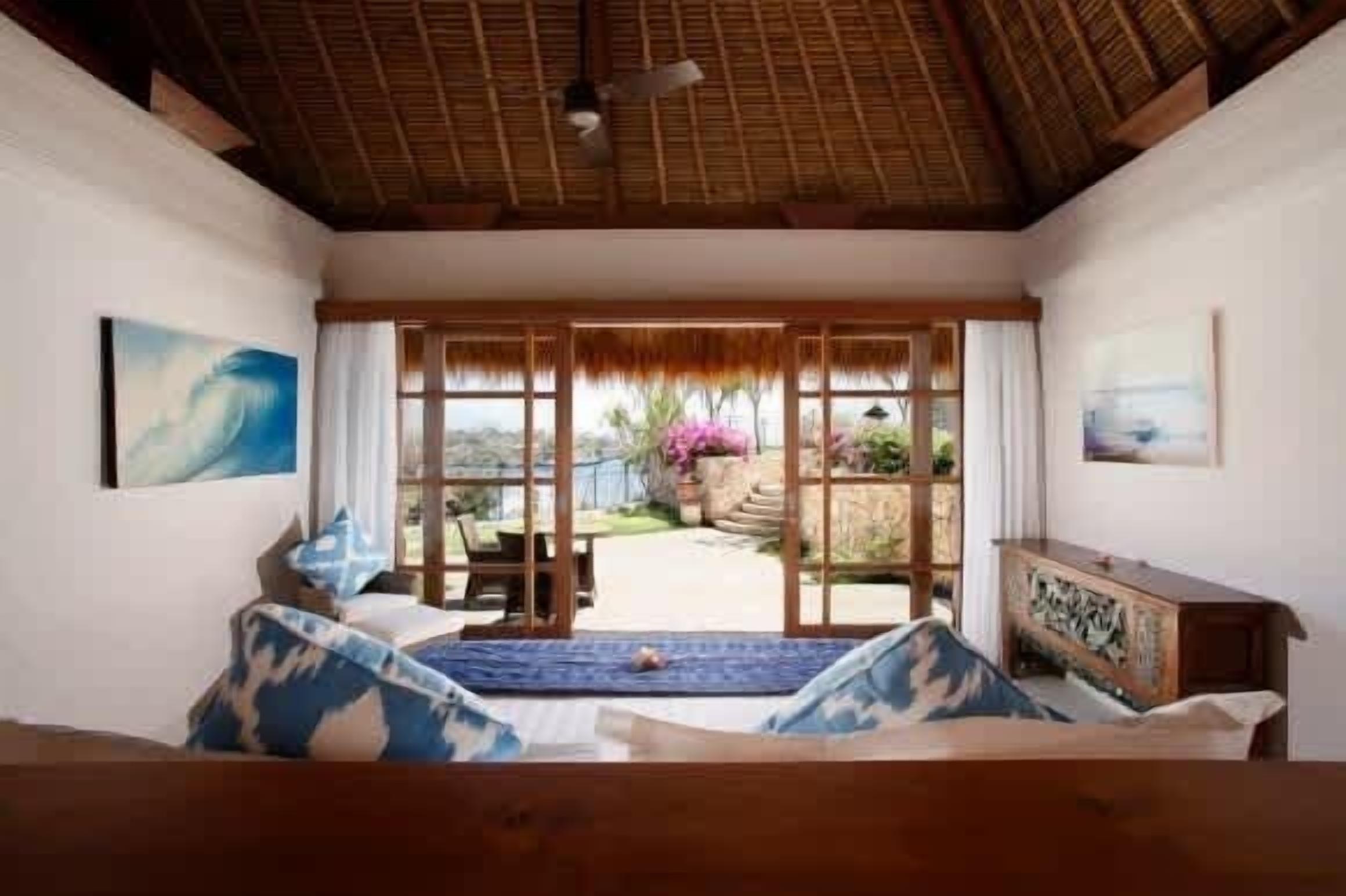 A room with a bed, a wooden bench, a table, and a view of a garden through a glass door.