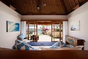 Ein Zimmer mit einem Bett, einer hölzernen Bank, einem Tisch und einem Blick auf einen Garten durch eine Glastür.