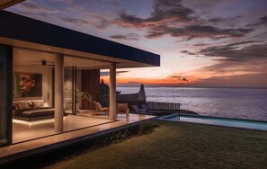 Ein modernes Haus mit einem Balkon mit Blick auf das Meer bei Sonnenuntergang.
