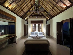 Ein Schlafzimmer mit einem großen Bett, einem Schreibtisch, einem Sessel, einem Deckenventilator und Blick durch eine offene Tür.