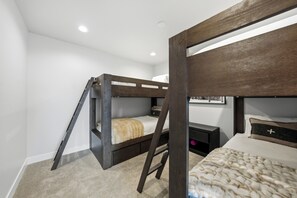 Une chambre avec un lit superposé, une échelle, une table de chevet et une étagère fixée au mur.
