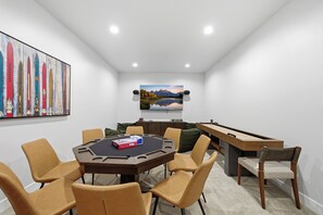 Une pièce avec une table ronde, des chaises, un billard, un tableau et un téléviseur accroché au mur.