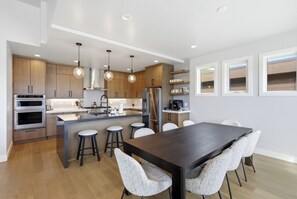 A modern kitchen with wooden cabinets, stainless steel appliances, and a central island with stools. - Sauna + Cold Plunge + Game Room | Jordanelle Views | Serenity Now (Hideout)