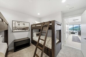 Une chambre moderne avec des lits superposés, un téléviseur fixé au mur et une grande fenêtre donnant sur l’extérieur.