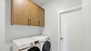 Une buanderie équipée de deux machines à laver Samsung blanches, de meubles en bois et d’une porte blanche.