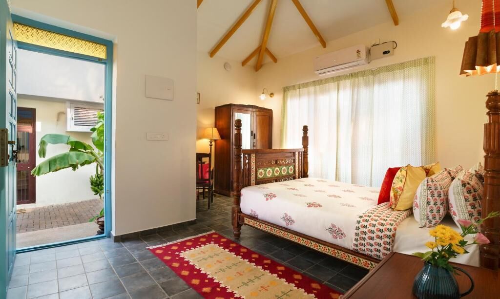 A bedroom with a bed, a wooden wardrobe, a nightstand, a lamp, and a window with curtains.