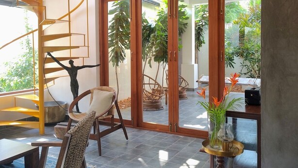 A modern interior with a spiral staircase, a dining area with wicker furniture, and a view of a garden through glass doors.