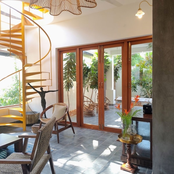 A modern interior with a spiral staircase, a dining area with wicker furniture, and a view of a garden through glass doors.