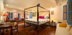 A four-poster bed in a room with a wooden floor, a dining table, a sofa, and a small table with a lamp. - Isai Karai Bungalow - A CGH Earth Saha (Tirupporur)