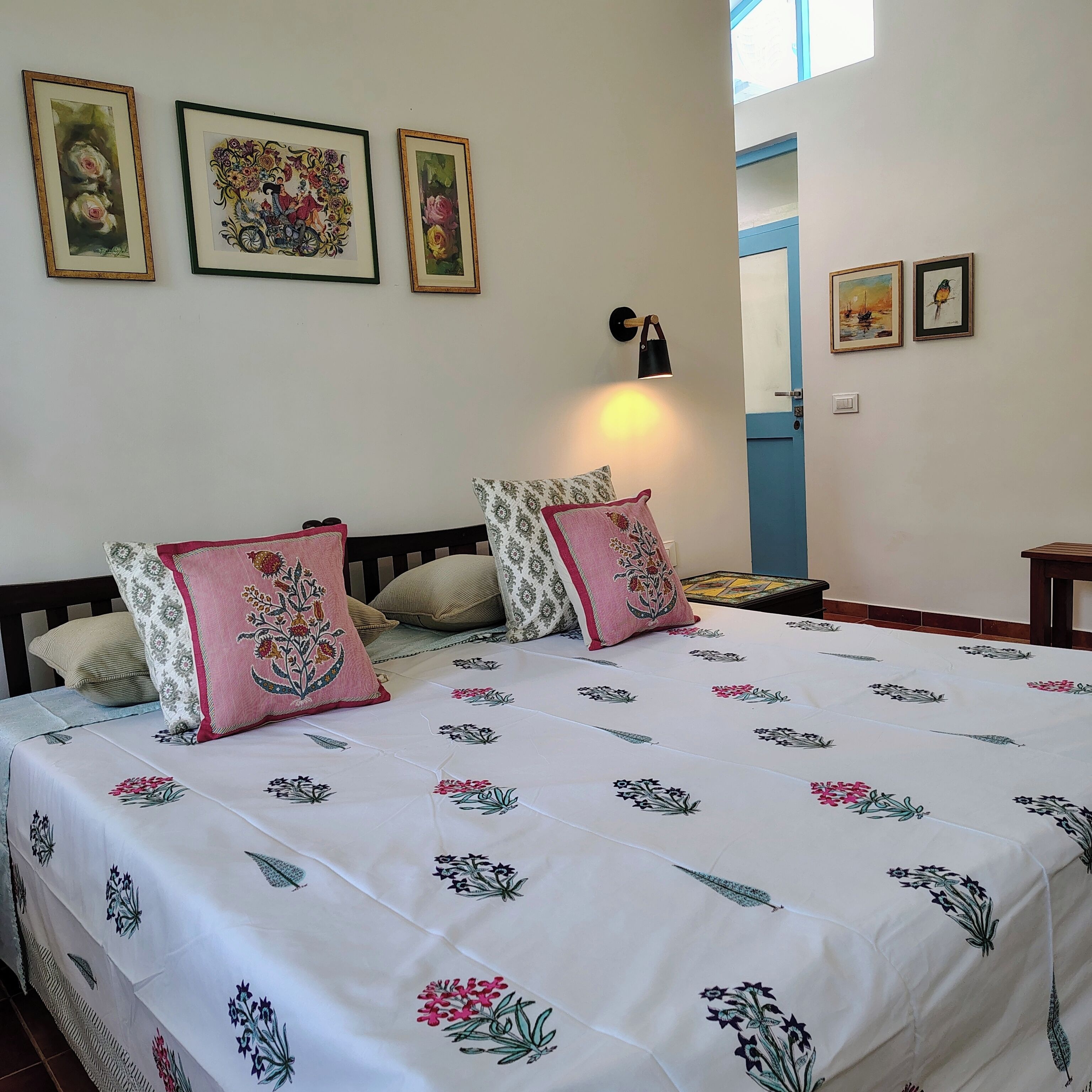Una cama doble con ropa de cama floral, una mesita de noche, una lámpara de pared y cuadros en la pared.