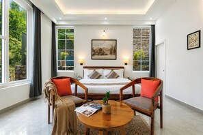 Un dormitorio con cama, dos sillones, una mesa y un ventanal con cortinas.