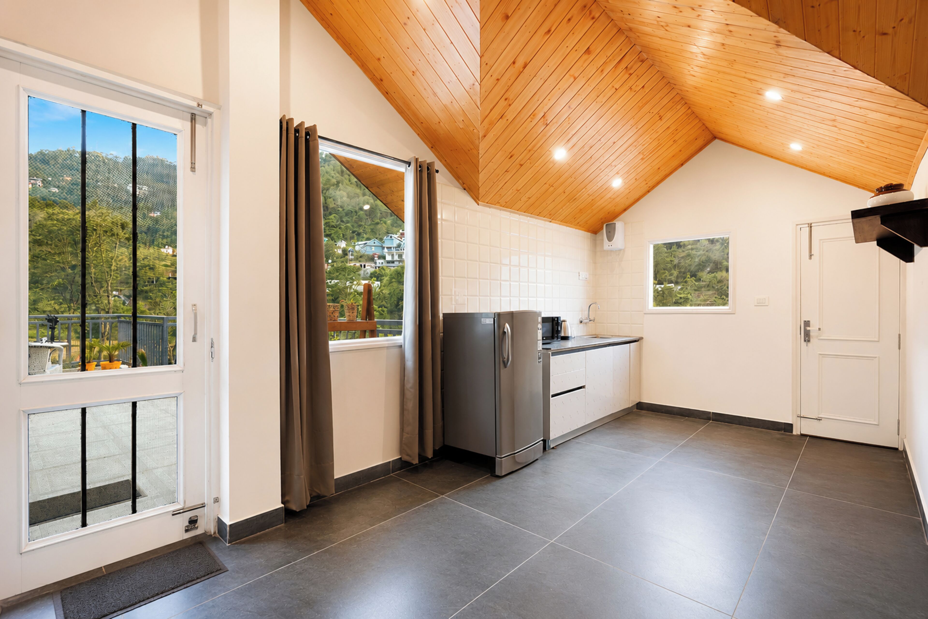 A kitchen with a view of a mountainous landscape, a wooden ceiling, and a stainless steel refrigerator.
