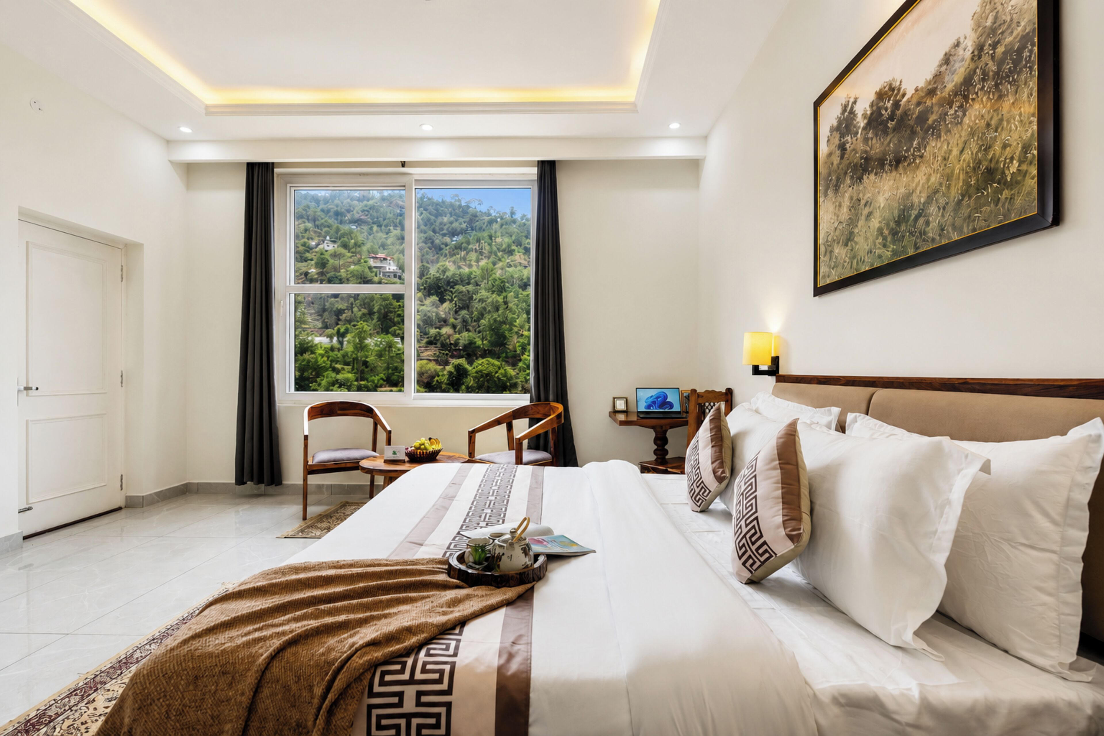 A hotel room with a large bed, a desk with a chair, a window with a view of greenery, and a painting on the wall.
