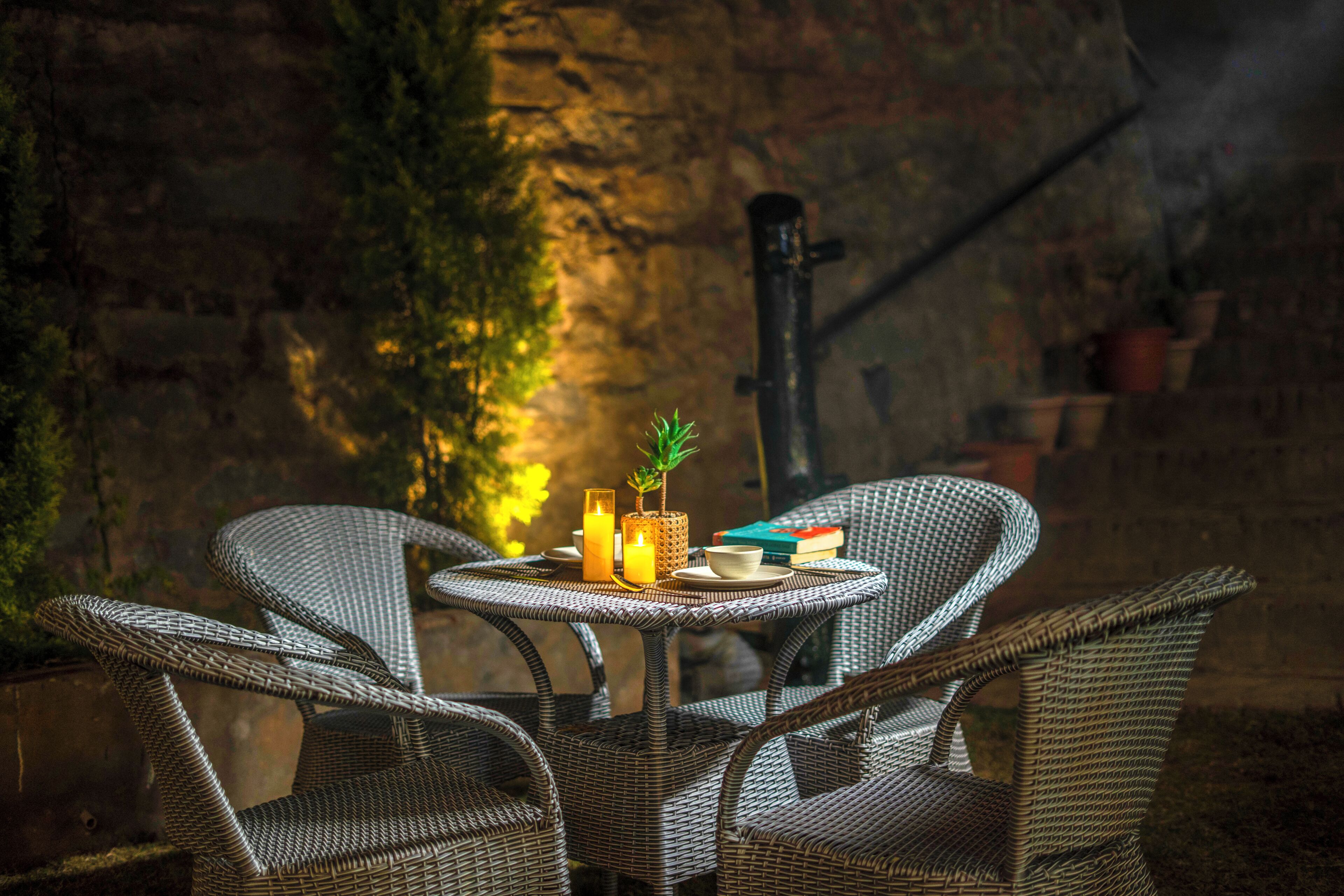Wicker chairs around a small table with candles, books, and a potted plant.