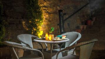 Wicker chairs around a small table with candles, books, and a potted plant.