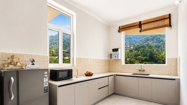 A modern kitchen with a refrigerator, microwave, and sink, a window with a view of greenery, and a bamboo blind. - Alaya Stays Gable Pine with Pool (Kasauli)