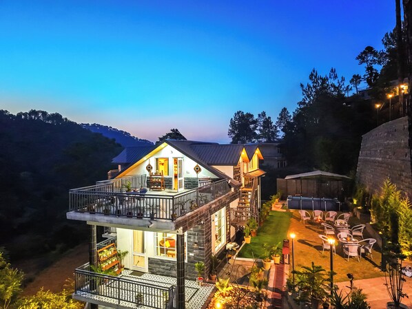 A two-story building with a balcony, outdoor seating, and a stone wall. - Alaya Stays Gable Pine with Pool (Kasauli)