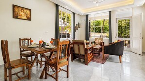 A dining area with wooden furniture, a Buddha painting, and a view of greenery through large windows. - Alaya Stays Gable Pine with Pool (Kasauli)