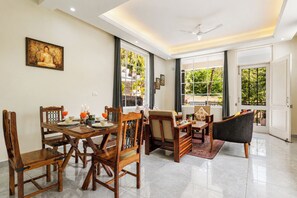 A dining area with wooden furniture, a Buddha painting, and a view of greenery through large windows. - Alaya Stays Gable Pine with Pool (Kasauli)