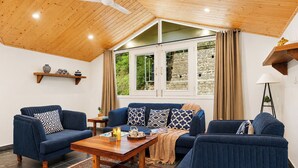 A room with a wooden ceiling, a sofa set, a coffee table, a lamp, and a view through a window. - Alaya Stays Gable Pine with Pool (Kasauli)