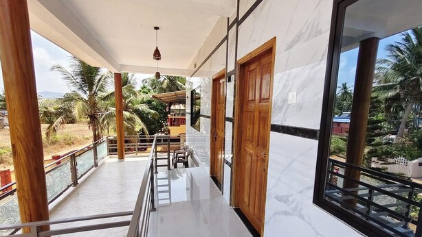 A balcony with a view of palm trees, a wooden door, and a metal railing. - Anthik Family Homestey (Bhatkal)
