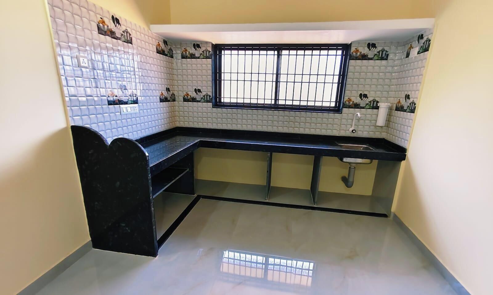 Una cocina con paredes de azulejos blancos, una encimera negra y una ventana con barrotes.