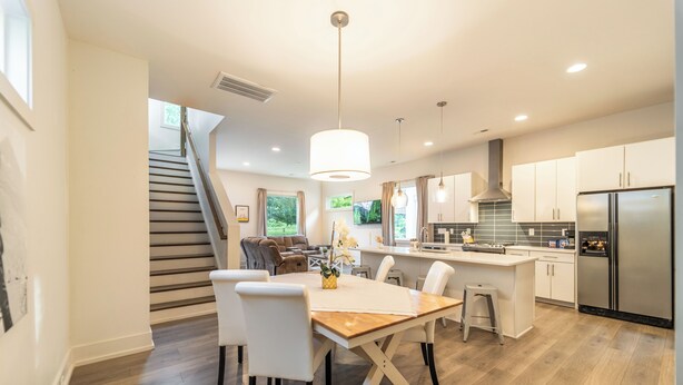 Une cuisine moderne avec un coin repas, un plancher en bois et un escalier menant à l’espace de vie.