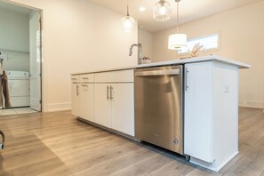Una cocina moderna con lavavajillas de acero inoxidable, armarios blancos e iluminación colgante.