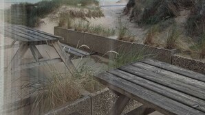 Une vue sur la plage avec un banc en bois, un chemin en béton et un lampadaire en métal.
