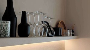 Une cuisine avec un évier noir, une planche à découper en bois, un vase avec des branches et un porte-verres à vin.