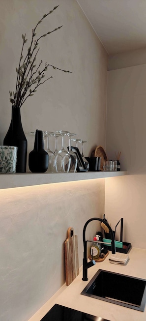 Eine Küche mit einem schwarzen Spülbecken, einem Holztisch zum Schneiden, einer Vase mit Zweigen und einem Weinkühler.