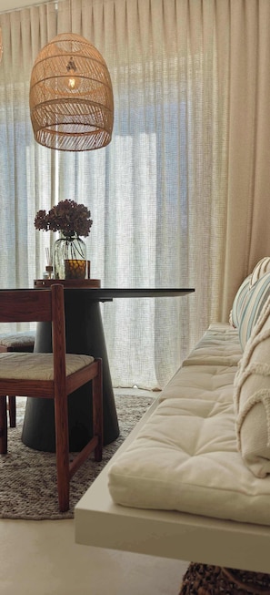 Ein Zimmer mit einer Couch, einem Holzsessel, einem Tisch mit einer Vase und einer Pendelleuchte.