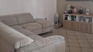 Una sala de estar con un sofá seccional color beige, un televisor de pantalla plana montado en la pared y un estante con objetos decorativos.