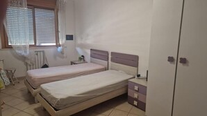 Un dormitorio con dos camas, un armario, un radiador y una ventana con persianas.